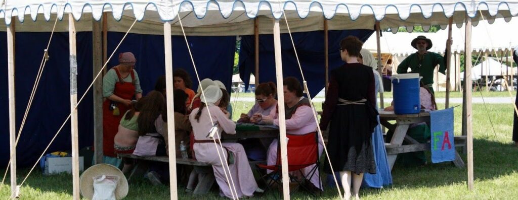 A bunch of SCA members sitting under a tent during a class.